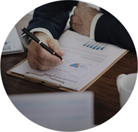 Ein Mann in einem dunklen Anzug hält einen Stift in der rechten Hand und zeigt auf ein Klemmbrett mit einem Finanzdokument. Auf dem Dokument sind Diagramme, Zahlen und ein Titel mit dem Wort „Financial Plan“ zu sehen. Im Hintergrund sind verschwommen weitere Unterlagen und eine Kaffeetasse auf einem Holztisch erkennbar. Die Szene vermittelt ein professionelles Arbeitsumfeld im Bereich Finanzen oder Buchhaltung.